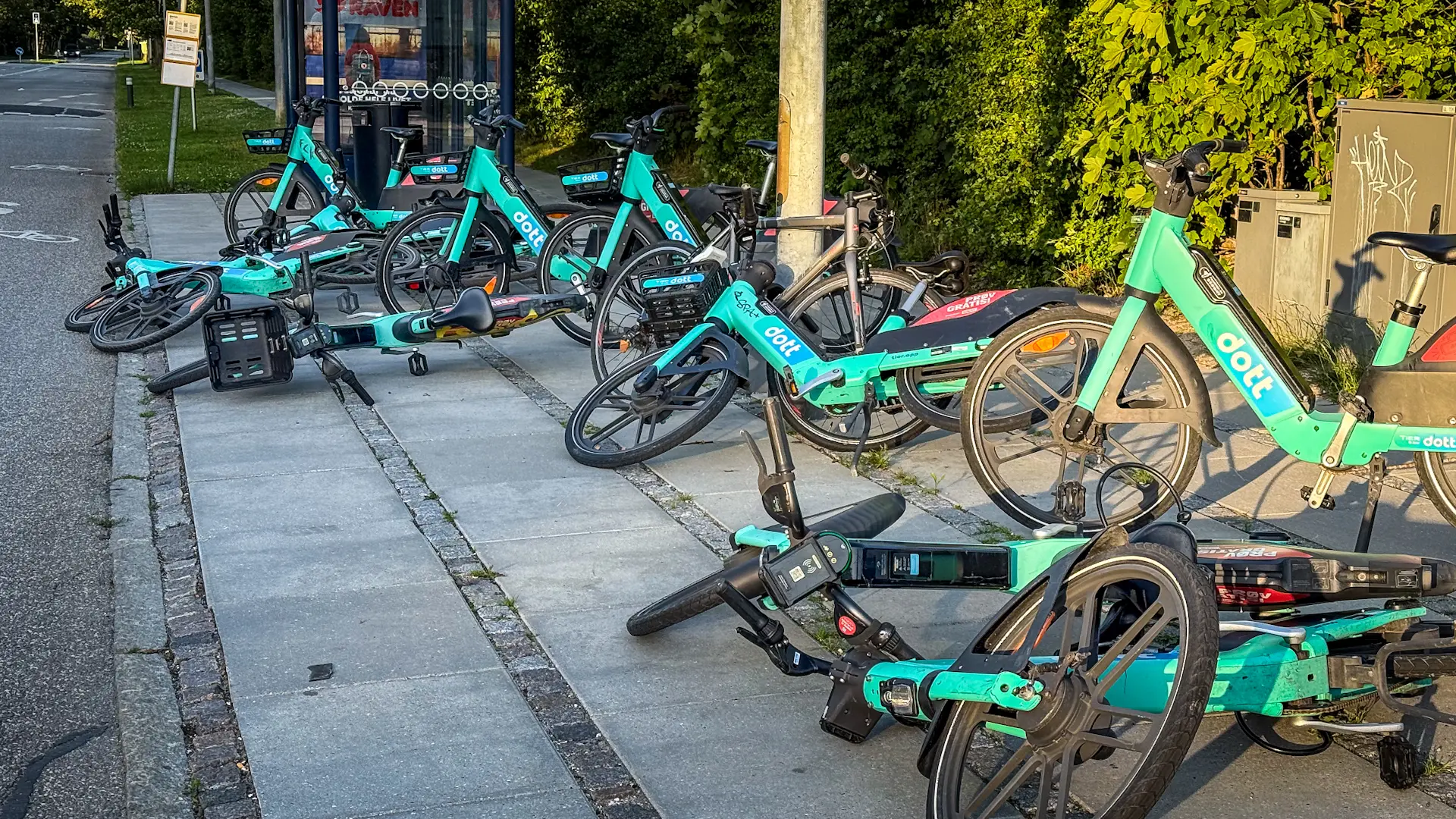 Henkastede lyseblå delecykler ligger spredt på fortov eller gadehjørne i Glostrup, hvilket illustrerer den æstetiske forringelse af byens udtryk